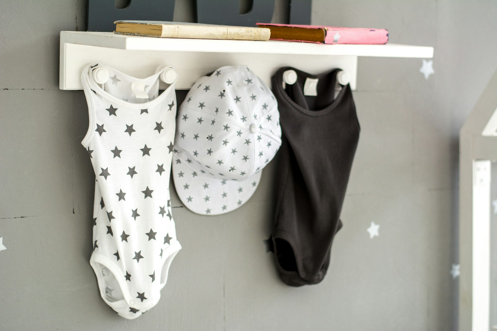 Baju bayi putih dan topi kecil digantung di dinding kayu
